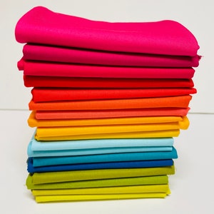 May include: A stack of 15 fabric squares in a rainbow color gradient, starting with pink and ending with yellow. The fabric is smooth and has a slight sheen.