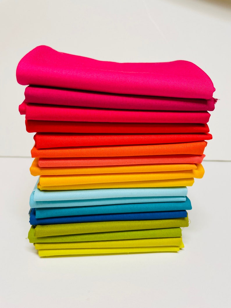 May include: A stack of 15 fabric squares in a rainbow color gradient, starting with pink and ending with yellow. The fabric is smooth and has a slight sheen.