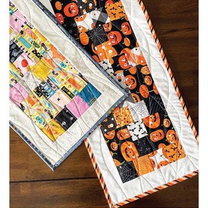May include: A Halloween-themed table runner sewing pattern featuring a patchwork design with orange, black, and white fabric. The pattern is called "Candy Crush" and is described as a "Table Runner Project" that is "Mini Charm & Scrap Friendly". The finished size is 12 inches by 42 inches.