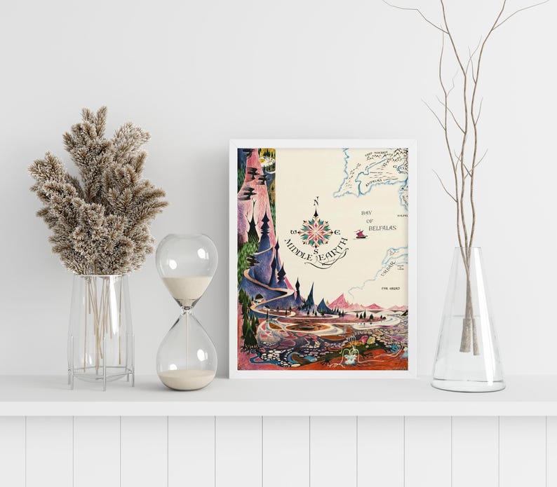 Pu&ograve; includere: Una stampa incorniciata di una mappa della Terra di Mezzo, con una rosa dei venti e illustrazioni dettagliate di paesaggi. L'opera d'arte &egrave; in una cornice bianca ed &egrave; esposta su una mensola bianca.