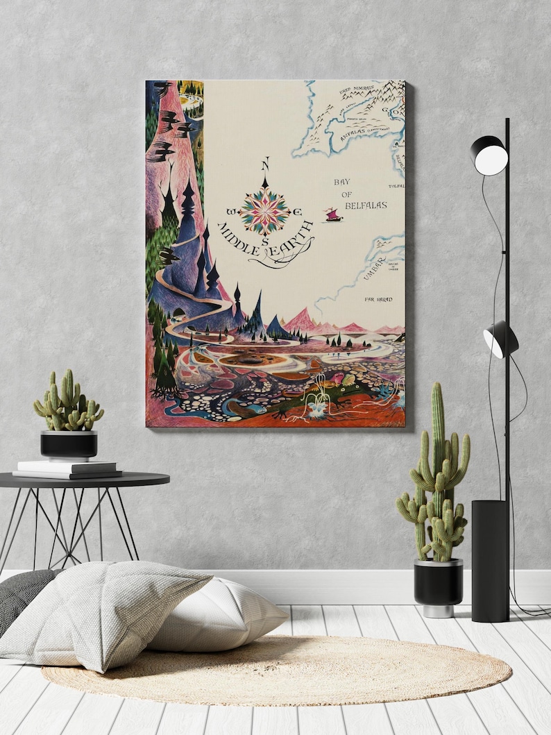Pu&ograve; includere: Una stampa della mappa della Terra di Mezzo con una rosa dei venti e illustrazioni dettagliate di paesaggi. L'opera d'arte presenta una tavolozza di colori di blu, verdi, rosa e arancioni. La mappa &egrave; esposta su una parete in una stanza con piante decorative e cuscini.