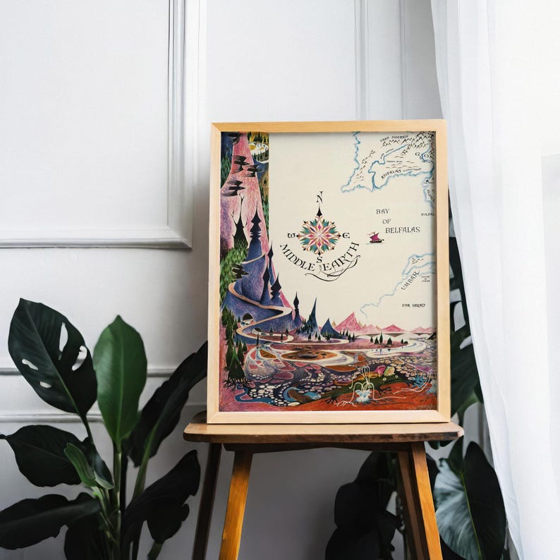 Pu&ograve; includere: Una stampa incorniciata di una mappa della Terra di Mezzo con una rosa dei venti. L'opera presenta un paesaggio colorato con montagne, fiumi e il testo "Middle Earth" e "Bay of Belfalas". La cornice &egrave; in legno chiaro.