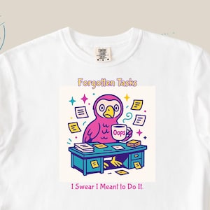 Puede incluir: Camiseta blanca con un gráfico colorido de un búho en un escritorio. El texto dice "Forgotten Tasks" y "I Swear I Meant to Do It." El búho es rosa y sostiene una taza de café. El escritorio es azul.