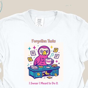Puede incluir: Camiseta blanca de manga larga con un gráfico de dibujos animados colorido. El gráfico presenta un búho rosa en un escritorio con el texto "Forgotten Tasks" y "I Swear I Meant to Do It."