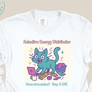 Puede incluir: Camiseta blanca de manga larga con un diseño de gato de dibujos animados. El gato turquesa se representa con un portátil, una taza de café y otros objetos. El texto de la camiseta dice "Selective Energy Distributor" y "Overstimulated? Nap It Off."