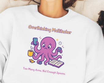 May include: A white crewneck sweatshirt featuring a graphic of a purple octopus with a sad expression. The octopus holds a smartphone, a yellow mug, and a multi-coloured cube. Text reads: Overthinking Multitasker. Too Many Arms. Not Enough Spoons.