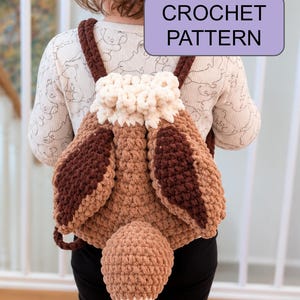 May include: A brown and cream crochet backpack featuring a plush animal design with long ears and a tail, accompanied by a purple rectangular label with the text CROCHET PATTERN in black letters, worn as a functional accessory with shoulder straps.