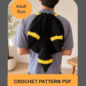 Może przedstawiać: Czarno-żółty plecak wykonany na szydełku z dwoma dużymi spiczastymi uszami i ogonem, z napisem Adult Size oraz CROCHET PATTERN PDF. Plecak jest noszony na plecach na szarym t-shircie, prezentując teksturowaną konstrukcję z włóczki.