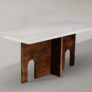 May include: A rectangular dining table featuring a thick, white marble top with subtle grey veining. The base is constructed from dark brown wood, consisting of two vertical panels, each featuring a distinct arched cutout design.