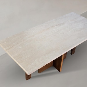 May include: A rectangular coffee table with a light-colored stone top and dark wood legs. The table's top is approximately 60 inches long and 30 inches wide. The legs are made of dark wood and are positioned at each end of the table.