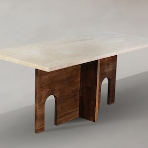 May include: A rectangular dining table featuring a smooth, light beige stone tabletop with natural veining. The base is constructed from dark brown wood panels, each featuring a distinct arched cutout design that supports the heavy top.