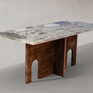 May include: A rectangular dining table featuring a multi-coloured terrazzo stone top with grey, white, and dark green flecks. The base is constructed from dark brown wood panels, each featuring a distinct arched cutout design on the sides.