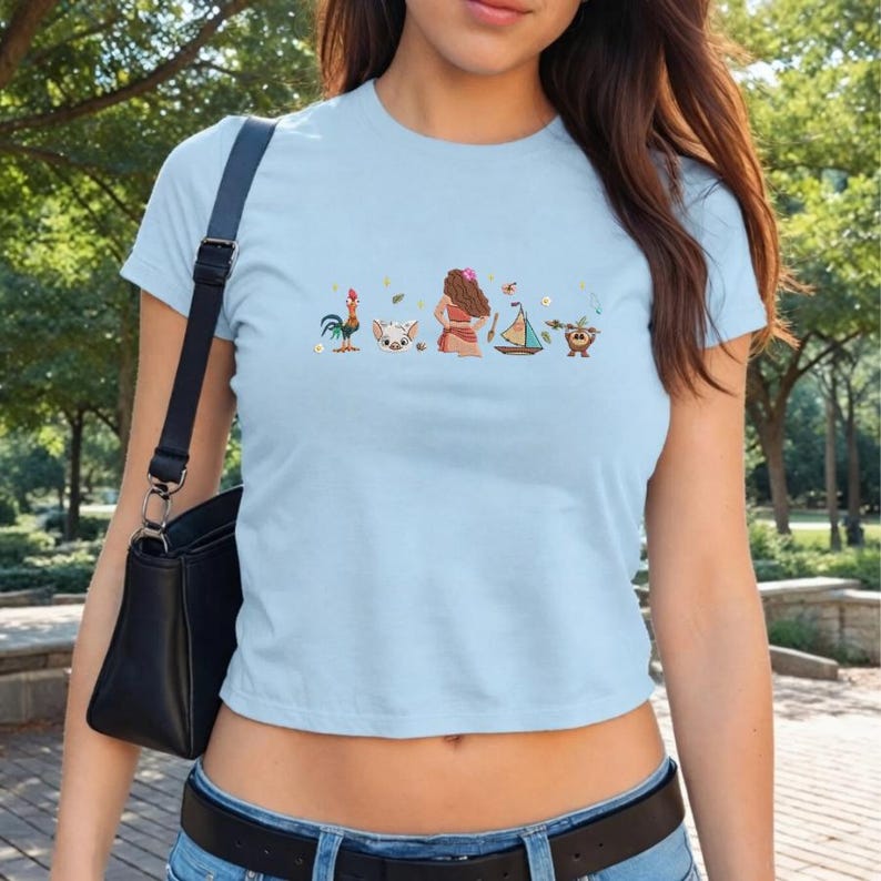Peut inclure: Haut court bleu clair avec un motif de personnages de dessins anim&eacute;s color&eacute;s. Le motif comprend un coq, un cochon, une femme, un voilier et un personnage de noix de coco. Le t-shirt est en mati&egrave;re douce et a des manches courtes.