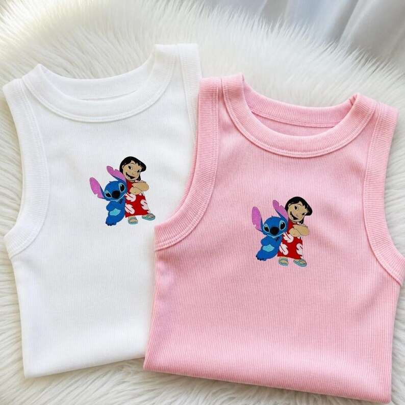 May include: Two ribbed tank tops, one white and one pink, featuring an embroidered image of Lilo and Stitch. The image shows Lilo in a red dress and Stitch in blue. The tops have a round neckline.