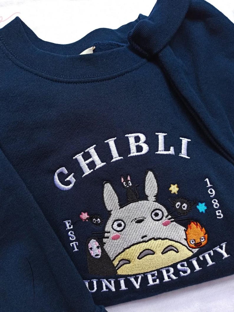 Pu&ograve; includere: Felpa blu navy con ricamo "Ghibli University". Presenta un personaggio dei cartoni animati con altre figure animate, il testo "EST 1985" e la parola "Ghibli" in bianco.