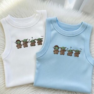 May include: Two sleeveless baby vests, one white and one light blue. Each vest features a graphic of a cartoon character in a brown robe with the text "cool!" and a question mark. The white vest is on the left, and the blue vest is on the right.