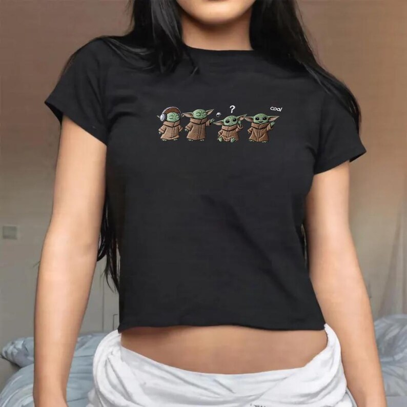 May include: Black crop top featuring a graphic of Baby Yoda in various poses. The design includes Baby Yoda with headphones, a question mark, and the word "cool". The shirt has short sleeves and a crew neck.