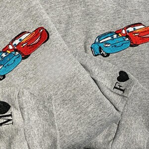 May include: Grey sweatshirt with embroidered cartoon cars in red and blue. The sleeves have embroidered hearts with the letters "M" and "F".