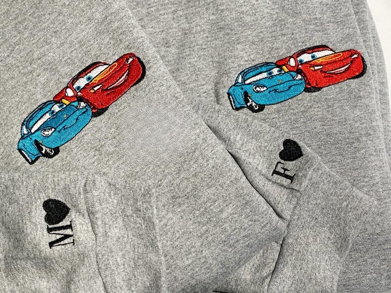 May include: Grey sweatshirt with embroidered cartoon cars in red and blue. The sleeves have embroidered hearts with the letters "M" and "F".