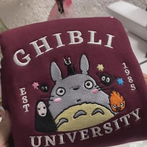Pu&ograve; includere: Felpa bordeaux con design ricamato. Il design presenta la scritta "GHIBLI" sopra un personaggio dei cartoni animati, con "UNIVERSITY" sotto. Il design include altri personaggi e l'anno "1985".