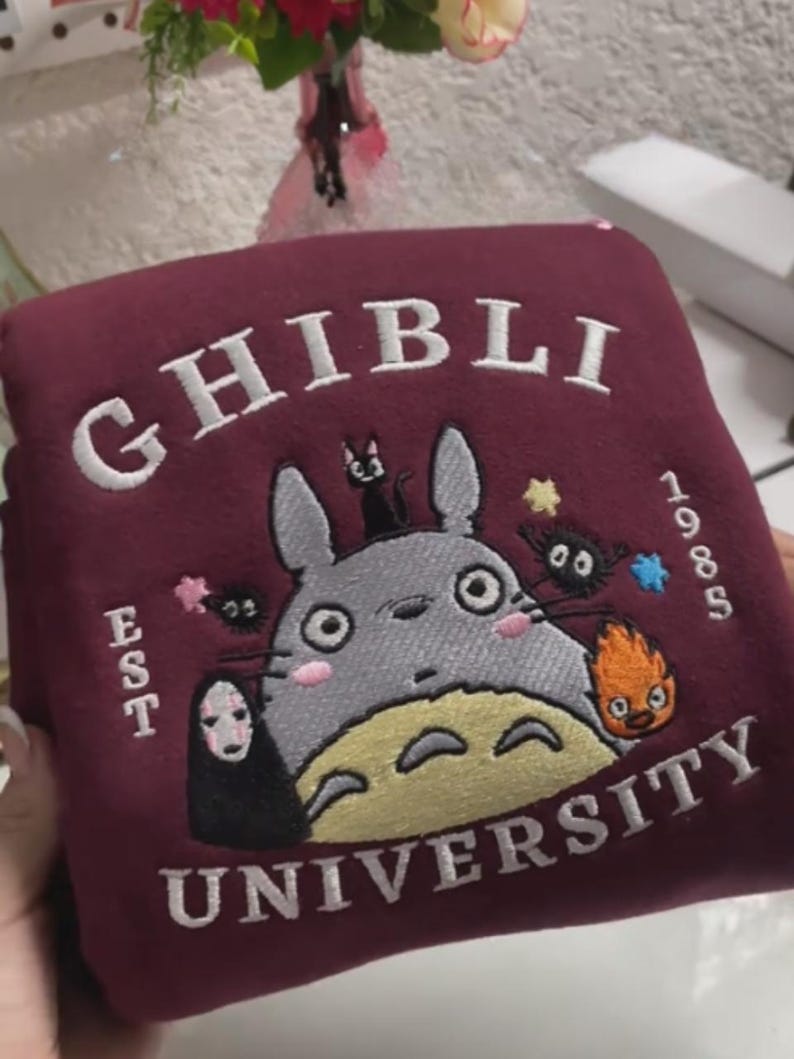 Pu&ograve; includere: Felpa bordeaux con design ricamato. Il design presenta la scritta "GHIBLI" sopra un personaggio dei cartoni animati, con "UNIVERSITY" sotto. Il design include altri personaggi e l'anno "1985".