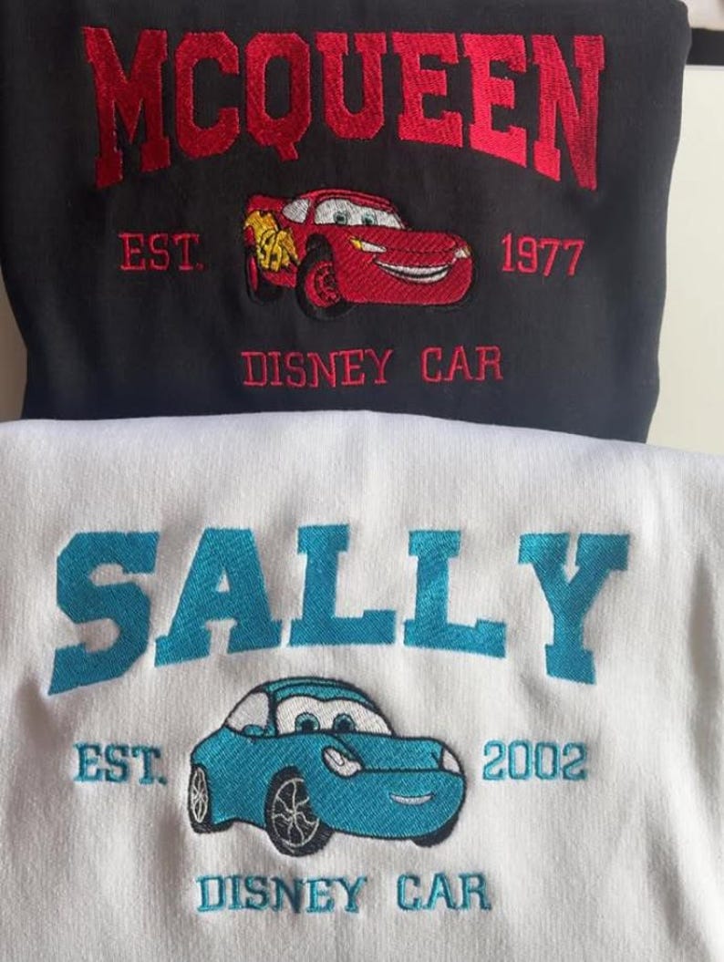 May include: Black sweatshirt with red embroidered text "MCQUEEN" above a red cartoon car and the text "DISNEY CAR". Below is a white sweatshirt with blue embroidered text "SALLY" above a blue cartoon car and the text "DISNEY CAR".