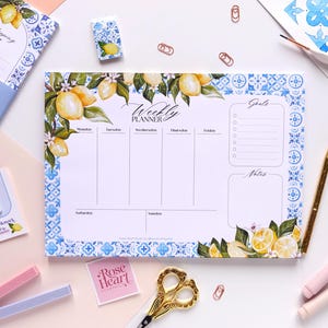 Può includere: Un blocco note per la pianificazione settimanale con un bordo di piastrelle mediterranee blu e bianche e illustrazioni di limoni gialli. Il layout include sezioni da lunedì a domenica, un elenco di obiettivi e un'area note con il testo Weekly Planner.