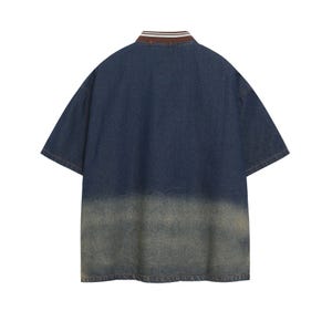 May include: A short-sleeved denim shirt with a faded, distressed appearance. The shirt features a brown and white striped collar and a two-tone design, transitioning from dark blue to a lighter, worn-out shade at the bottom. The back view is shown.