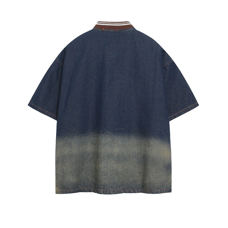 May include: A short-sleeved denim shirt with a faded, distressed appearance. The shirt features a brown and white striped collar and a two-tone design, transitioning from dark blue to a lighter, worn-out shade at the bottom. The back view is shown.