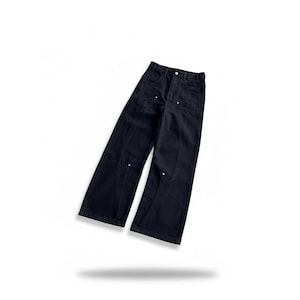 Puede incluir: Pantalones vaqueros azul marino oscuro con un dise&ntilde;o de pernera ancha. Los pantalones presentan detalles de costura blancos y peque&ntilde;os remaches blancos. La prenda se muestra sobre un fondo blanco.