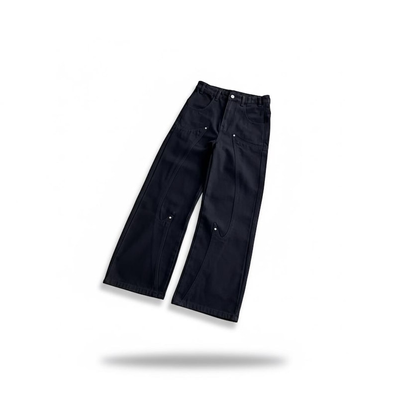 Puede incluir: Pantalones vaqueros azul marino oscuro con un dise&ntilde;o de pernera ancha. Los pantalones presentan detalles de costura blancos y peque&ntilde;os remaches blancos. La prenda se muestra sobre un fondo blanco.