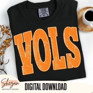 Puede incluir: Camiseta negra con la palabra "VOLS" en naranja, con letras desgastadas. La camiseta tiene cuello redondo y una etiqueta que dice "Comfort Colors". Las palabras "DESCARGA DIGITAL" están impresas en negro en la parte inferior de la imagen.