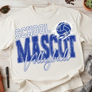 K&ouml;nnte beinhalten: Cremefarbenes T-Shirt mit den Worten "SCHOOL MASCOT Volleyball" in Blau und Wei&szlig;. Eine blaue Volleyball-Grafik befindet sich auf der rechten Seite. Das Shirt ist aus einem weichen Material.