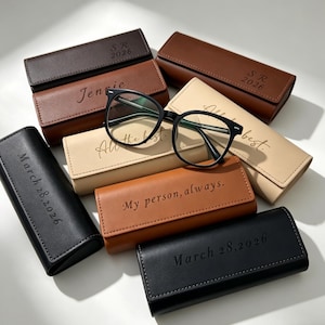 Pode incluir: Uma variedade de estojos de óculos personalizados em várias cores, incluindo preto, castanho e bege. Cada estojo apresenta texto personalizado, como nomes, datas e frases como "All the best" e "My person, always". Um par de óculos com armação preta repousa em cima.