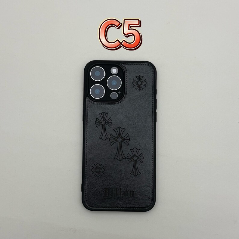 Pu&ograve; includere: Custodia per telefono nera con un design a croce e il nome "Dillon" in basso. La custodia ha un ritaglio per la fotocamera e il testo "C5" in un adesivo rosso e bianco sopra la custodia.