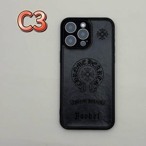 May include: Black leather phone case with embossed Chrome Hearts logo and the name "Rachel". The case has a stitched border and a camera cutout. A red and orange "C3" sticker is in the upper left corner.