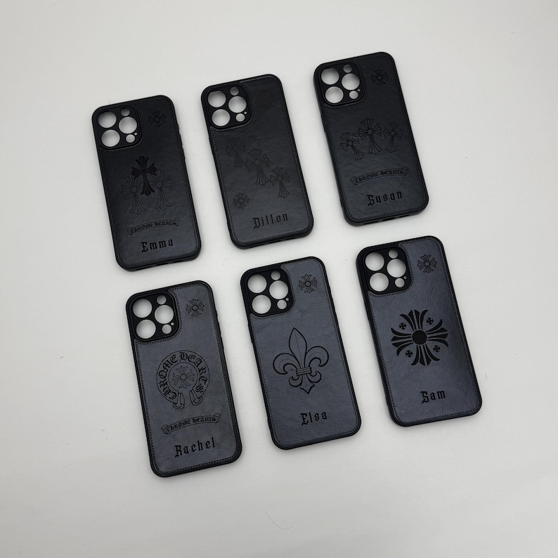 May include: A collection of six black phone cases with various embossed designs, including crosses, fleur-de-lis, and a heart emblem. Each case features a different name: Emma, Dillon, Susan, Rachel, Elsa, and Sam.