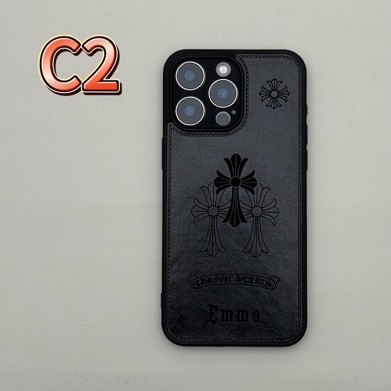 May include: Black leather phone case with embossed cross and floral designs. The case features the text "Chrome Hearts" and the name "Emma". The case has a camera cutout and a stitched border. A red and orange "C2" logo is in the upper left corner.