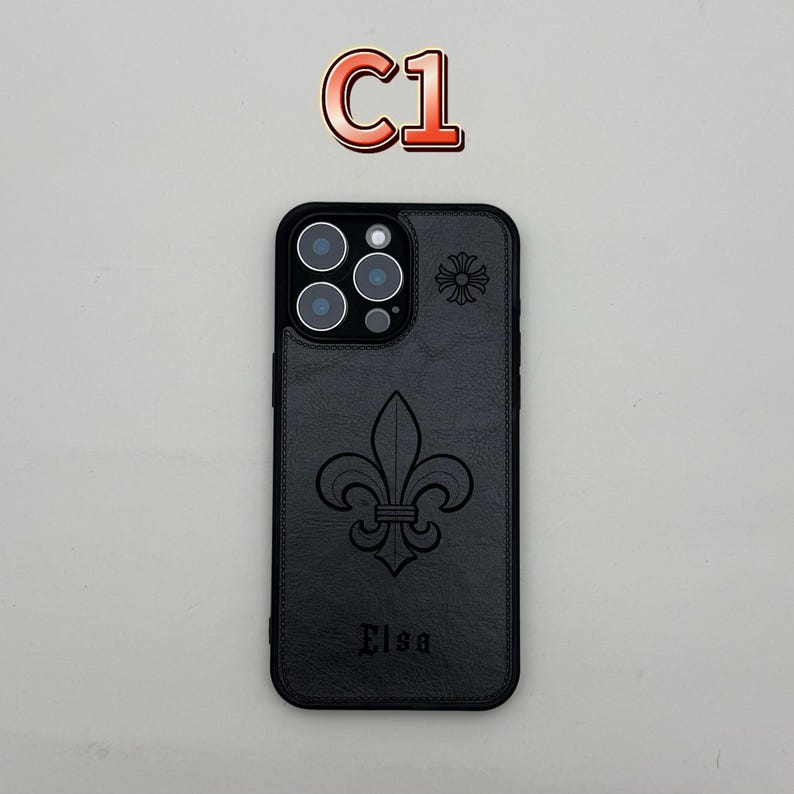 Pu&ograve; includere: Custodia per telefono nera con un design a giglio e il nome "Elsa" in rilievo in basso. La custodia presenta un motivo floreale vicino alla fotocamera e il testo "C1" in alto.