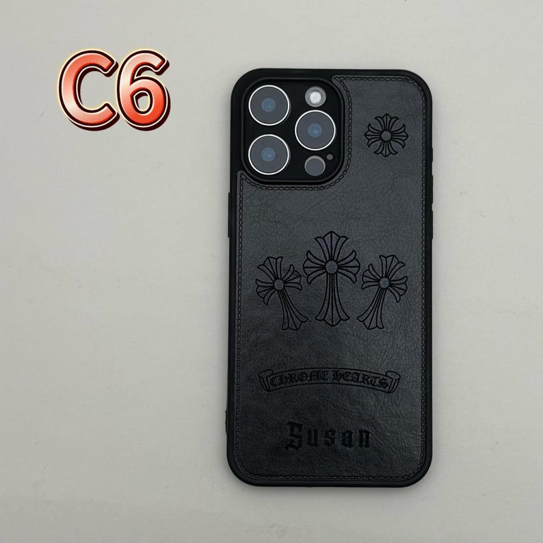 May include: Black phone case with embossed cross designs and the text "CHROME HEARTS" and "Susan". The case has a black camera lens surround and a stitched leather-like texture. The upper left corner has the text "C6".