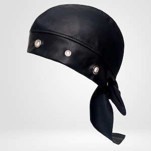 May include: A black head wrap featuring a smooth, matte finish and a wide band across the front. The band is accented with three visible silver-toned metal grommets. The back of the head wrap includes two long fabric ties that hang downward.