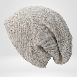 May include: A beige and brown speckled knit beanie hat. The hat is made of a soft, textured material and has a slouchy fit. The hat is a neutral color and can be worn by anyone.