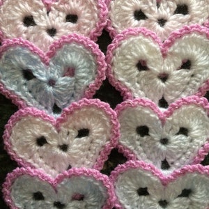 May include: Eight crocheted hearts in pink, white and blue with a pink sparkly trim. The hearts are arranged in two rows of four.