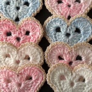 May include: Six crocheted hearts in pink, blue and white with gold trim. The hearts are arranged in two rows of three.