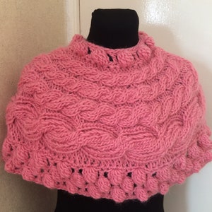 May include: A pink knitted shawl with a cable knit pattern and a crocheted border with bobbles.