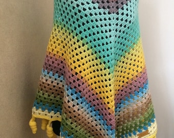 Peut inclure: Un poncho en crochet arc-en-ciel avec des glands jaunes. Le poncho est réalisé avec un point de granny square et a un col jaune clair.