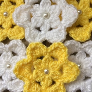 Könnte beinhalten: Eine Sammlung gehäkelter Blumen in Gelb und Weiß mit Perlen in der Mitte jeder Blume.