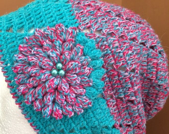 May include: A crocheted beanie hat in teal and pink with a pink and white crocheted flower embellishment and teal beads.