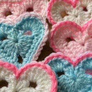 May include: A collection of crocheted hearts in pink, white and blue. The hearts are made with a delicate stitch pattern and have a soft, fluffy texture.