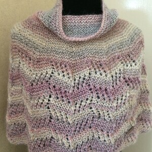 May include: A soft, knitted shawl with a delicate lace pattern in shades of pink, white, and grey. The shawl has a high neck and a flowing design.